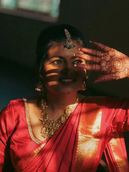 An artistic shot of a bride peeking through her fingers. The play of light and shadow across her face and henna-covered hand creates a mysterious and beautiful portrait.
