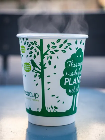 A steaming hot cup of coffee in a branded eco-cup. The visible steam instantly communicates warmth and comfort, perfect for a winter's day.