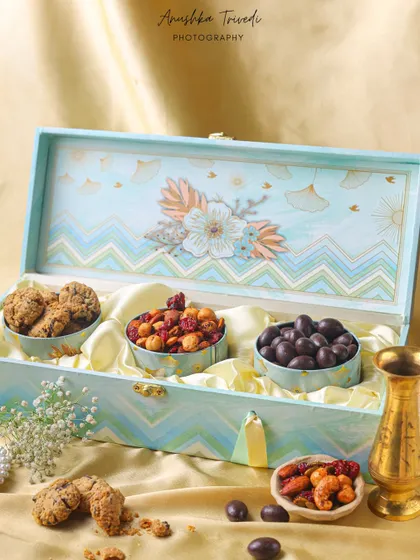 A pastel blue Diwali hamper filled with cookies and chocolates, styled with a golden diya for a soft and elegant festive look.