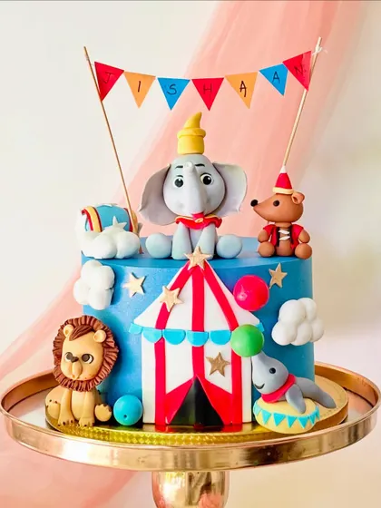 A colourful two-tiered circus cake featuring Dumbo. The cake is decorated with a circus tent, a lion, a seal, and other fun details.