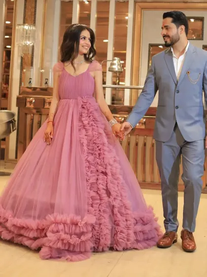 A couple holds hands in an elegant indoor setting. The client wears our pink ruffled gown, a perfect choice for an engagement or pre-wedding event.