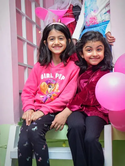 Say cheese! Two friends sit together in our playhouse, surrounded by pink balloons and smiling for the camera.