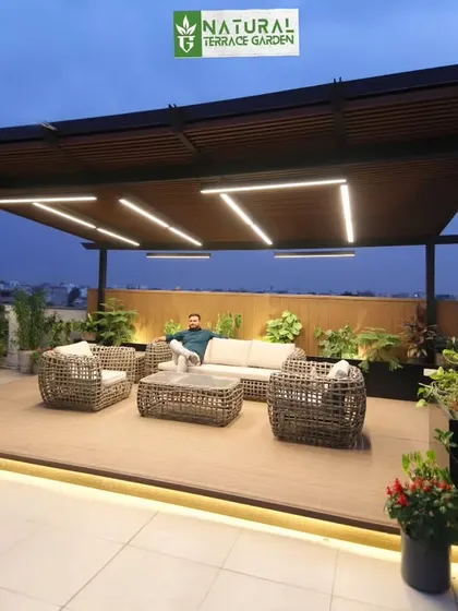 An evening shot of the Gurgaon Palam Vihar project, showing a person relaxing in the beautifully lit pergola lounge.