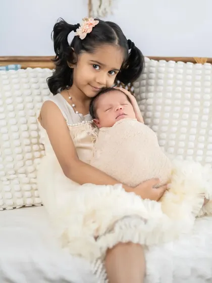An older sister proudly holds her new baby sibling. We ensure a safe and comfortable environment for sibling photos, creating memories of their very first moments together.