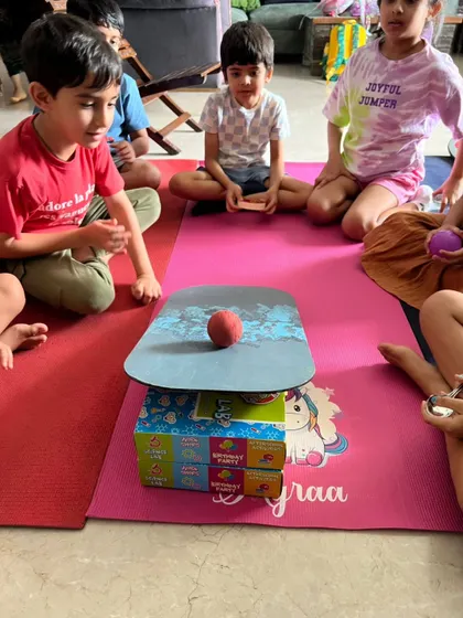 Kids watch intently as they test a balancing structure, learning about center of gravity and stability in this simple engineering challenge.