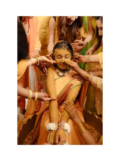 The bride being lovingly covered in Haldi by her family and friends. Her expression is one of pure joy.