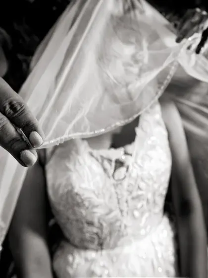A close-up, black and white shot of the veil being placed, focusing on the hands and the delicate fabric.
