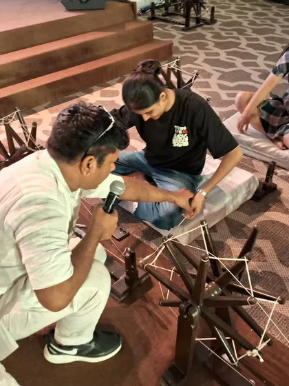 A student gets a personal lesson in spinning cotton on a charkha at the FDCI Khadi event, connecting with the roots of Indian textiles.