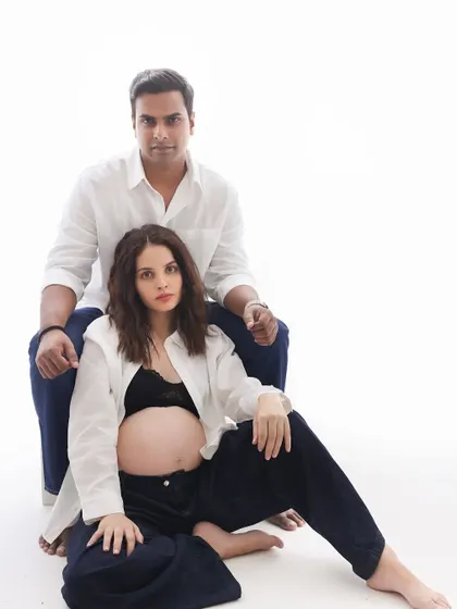 A modern family portrait. The couple's direct and confident gaze at the camera, combined with their chic, simple outfits, makes for a powerful image.