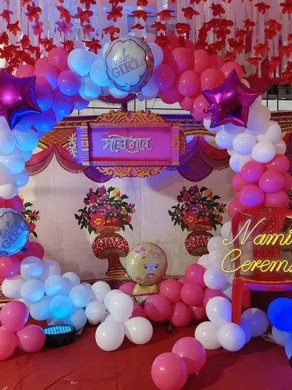A lovely naming ceremony decoration with a pink and white balloon arch. The setup includes a "Naming Ceremony" neon sign and traditional elements for a blessed occasion.