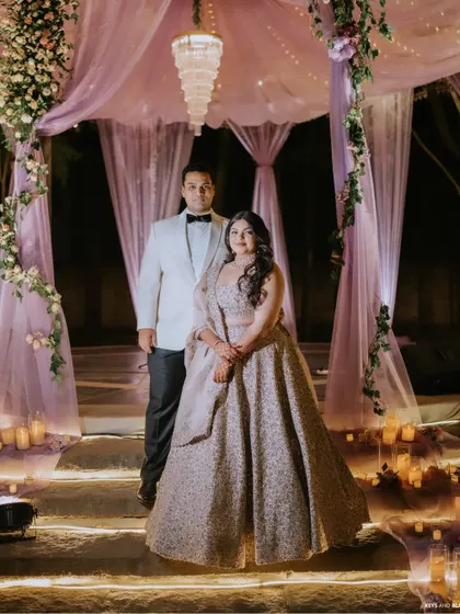 A portrait of elegance. The couple poses under a canopy of soft lavender drapes and a crystal chandelier, a romantic and dreamy setting we created for their cocktail party.