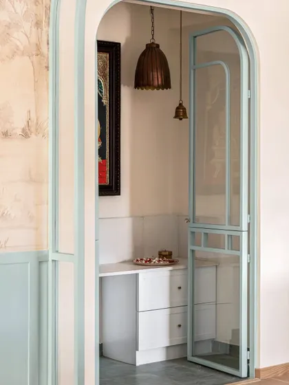 We created a serene puja nook off the dining area, framed by custom glass and metal doors painted in the same duck egg blue. This provides a quiet, dedicated space for prayer that is beautifully integrated into the home's design.