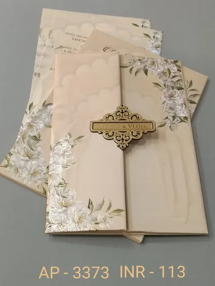 A beautiful gate-fold invitation in a creamy beige, decorated with white lilies and a wooden nameplate. The design is soft, elegant, and comes with three matching inserts.