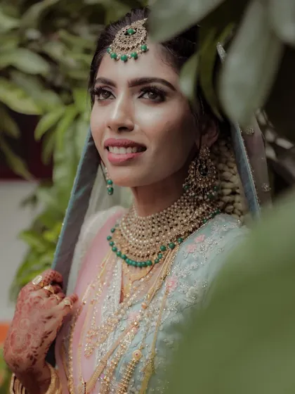 A beautiful portrait of the bride framed by green leaves, her gentle smile and elegant jewelry making for a captivating shot.