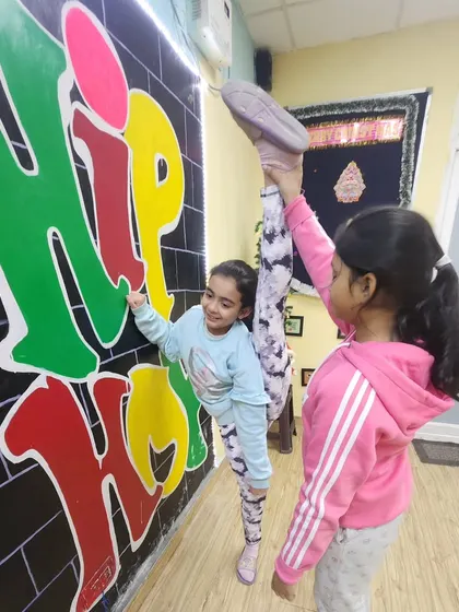 Practice makes perfect. Two young students work together on their wall-assisted splits, smiling and having fun while improving their flexibility.