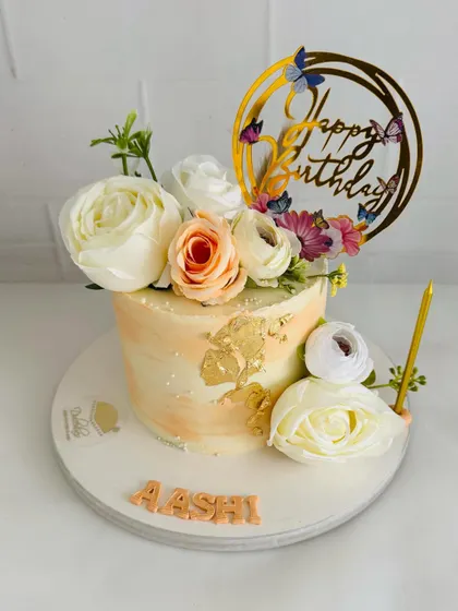 A lovely birthday cake with a soft peach watercolor effect, gold leaf, and fresh flowers.