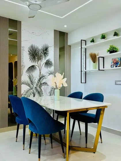 A modern dining area setup with plush blue velvet chairs, a marble-top table, and a feature wall with wallpaper and fluted panels.