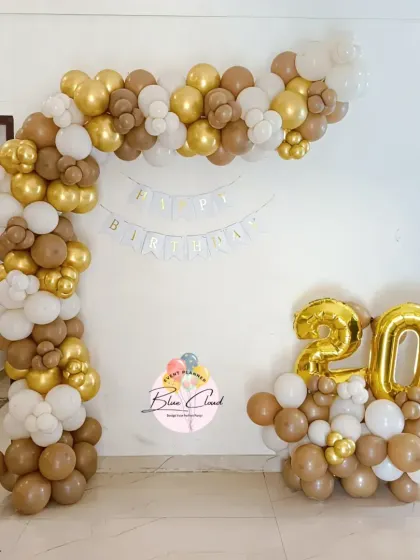 A sophisticated balloon arch in brown, gold, and white for a 20th birthday celebration at home.
