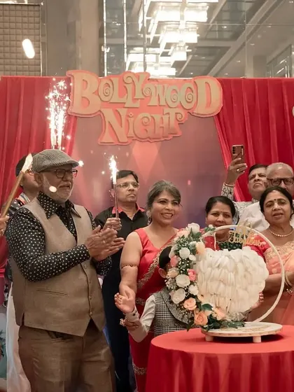 Another view of the joyous cake-cutting, with the 'Bollywood Night' backdrop setting the scene.