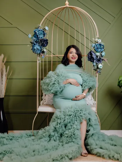 This mom-to-be looks absolutely serene in a mint green mermaid-style maternity gown. The studio setup with the golden birdcage chair and floral decor creates a beautiful, elegant portrait.