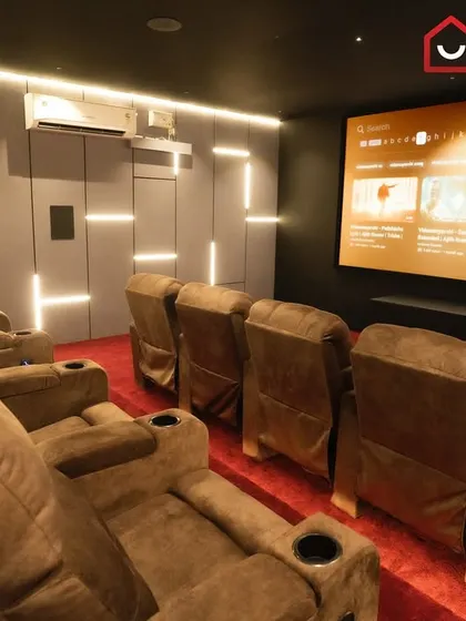 This 9.1.4 luxury home cinema in Thirunagar, Madurai, features plush brown recliners, a vibrant red carpet, and a geometric lighting pattern on the walls for a bold, modern look.