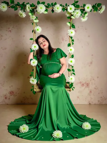 A peaceful portrait of a mom-to-be in a green gown, resting on a swing adorned with white flowers. The textured backdrop adds depth to this studio shot.