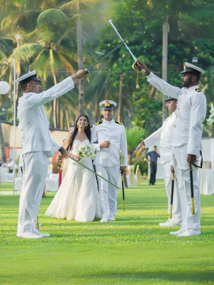 A wide shot of the impressive Arch of Sabers ceremony at a Navy wedding, set against a lush green lawn and palm trees.