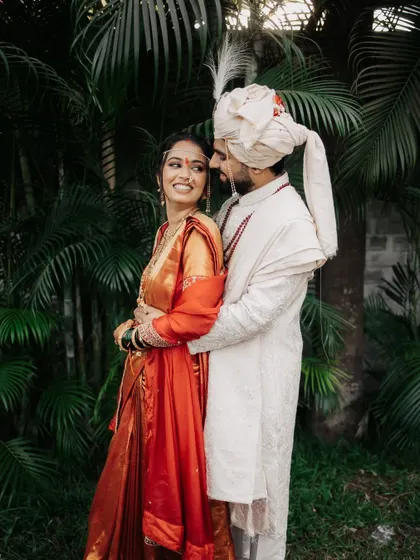 A classic, happy portrait of the Maharashtrian couple standing together against a lush, green background.