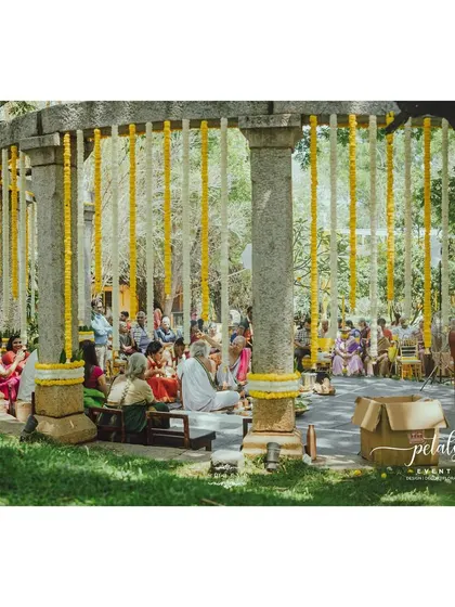 The stone pillars of the venue are decorated with hanging garlands of marigolds and chrysanthemums, with metal bells adding a touch of charm.