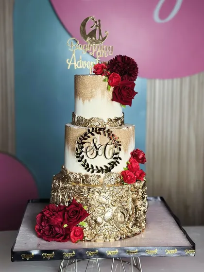 Love is in the details. This golden and red wedding cake radiates warmth and regal charm, featuring a dramatic gold-leafed bottom tier and crowned with rich red sugar roses.