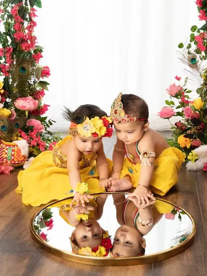Double the trouble, double the cuteness! These twin babies dressed as Krishna and Radha, discovering their reflections, is a moment of pure magic.