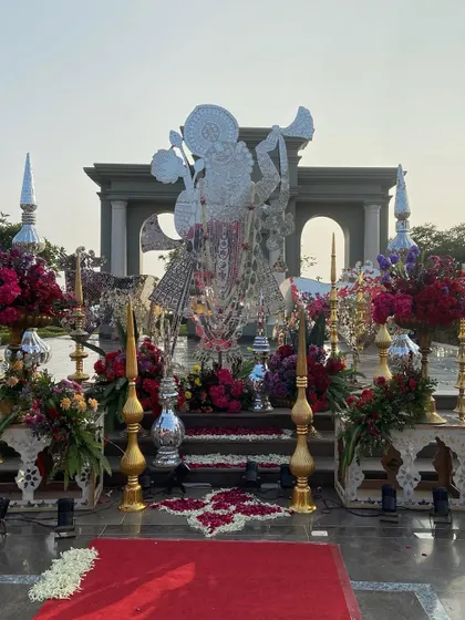 The divine presence of a Shreenathji sculpture, crafted in silver, stands as the centerpiece of this traditional ceremony. It is surrounded by vibrant floral arrangements, blending devotion with magnificent decor.