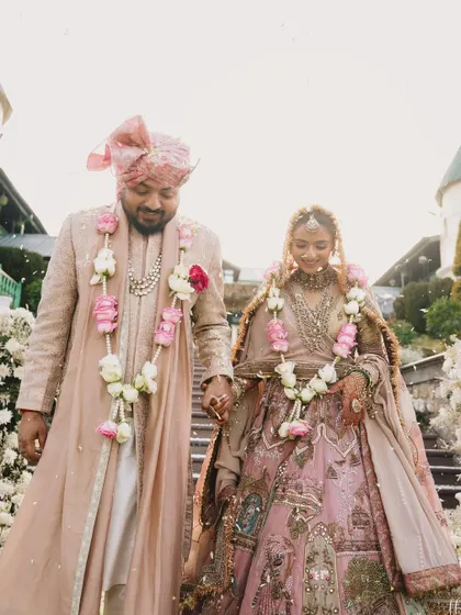 Walking down the steps together, their outfits blend seamlessly with the romantic, flower-filled setting. This is what perfectly coordinated couple styling looks like.