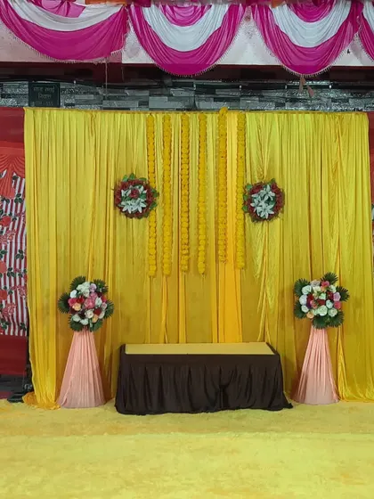A simple and elegant Haldi backdrop with yellow drapes and marigold flower strings. This is a classic look that is always beautiful.