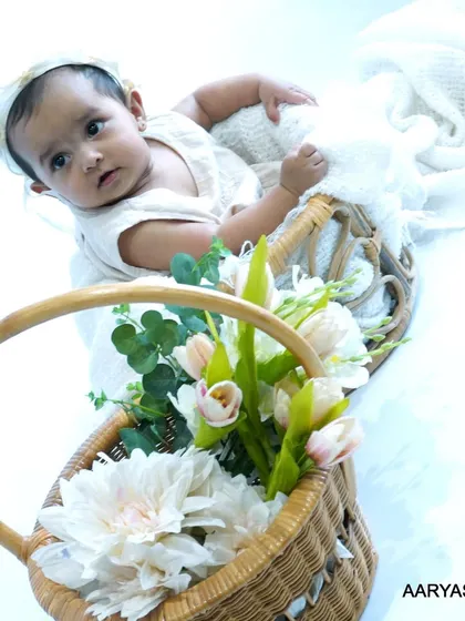 A baby poses in a basket setup that includes a second basket filled with beautiful white flowers. This composition adds depth and a touch of nature to the newborn portrait.