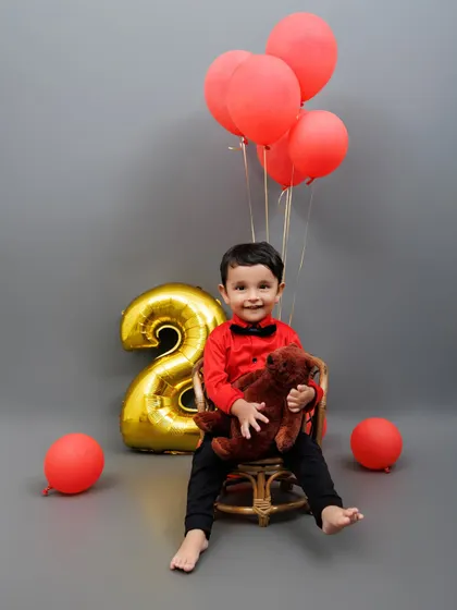 Two cute to handle! A stylish toddler celebrates his second birthday with red balloons and a teddy bear.