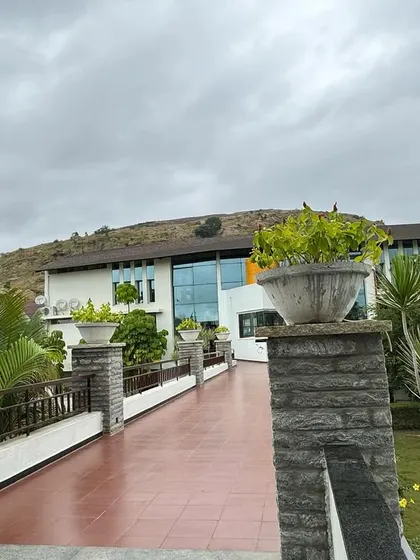 The walkway leading to our main building is flanked by lush greenery and stone pillars. This path marks the beginning of your journey from the outside world into a sanctuary of peace.