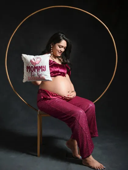 A playful and sweet pose using our studio props. The mom-to-be holds a "Mommy to be" cushion while seated within a golden ring, creating a modern and charming photograph.