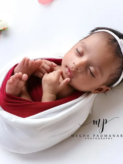 A close-up of a sleeping baby girl in a white wrap and headband, showcasing her beautiful, serene features.