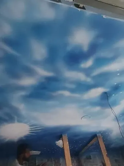 A dreamy sky mural painted on a ceiling, complete with clouds, sun, and stars, to create an illusion of looking up at an open sky.
