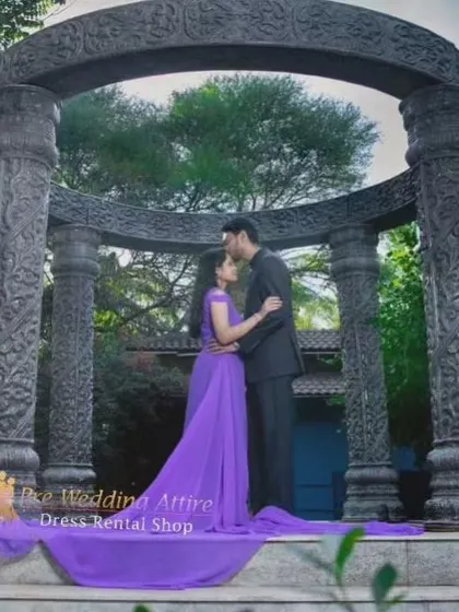 A romantic silhouette of a couple under a stone arch. The purple trail gown drapes elegantly down the steps, adding to the grandeur of the scene.