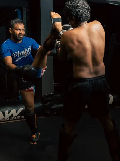 A fighter practices a high kick on a coach holding pads, showcasing flexibility and control.