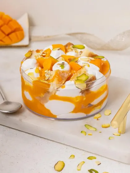 A mango tres leches style tub dessert, with whipped cream and pistachios, looking light and delicious.