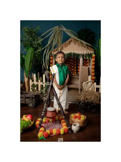 A wide shot of the little boy standing proudly in the complete Pongal festival set.