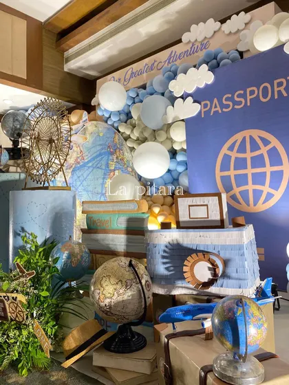 A detailed corner of a travel-themed party, featuring vintage-style globes, books, a piñata, and a large passport backdrop.