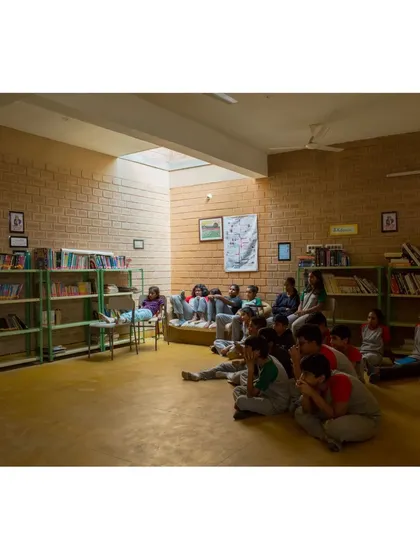 Students gather in the library at Buddhi School, illuminated by a large skylight. The space is designed to be a cozy and inviting corner for reading and quiet learning.