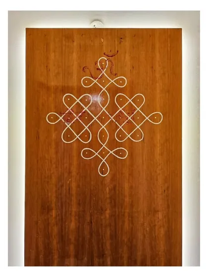 A close-up of the hand-painted Kolam, showing the clean, continuous lines that create the intricate, auspicious design against the warm wood grain.