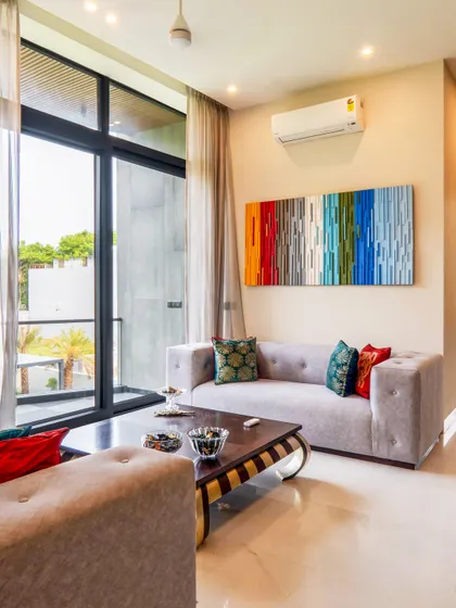 This drawing lounge in a modern farmhouse is where vibrant vibes meet chic design. Pops of color from the artwork and cushions contrast with the neutral sofa and large windows that look out onto the green landscape.