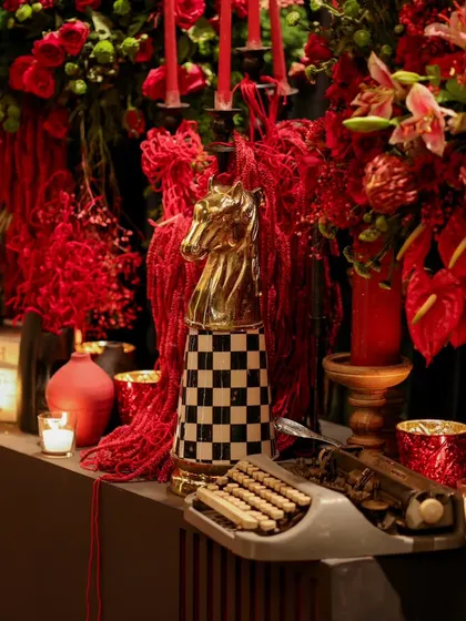 Eclectic decor elements like a vintage typewriter and a checkered chess piece are combined with red florals and candlelight to create intriguing, story-rich vignettes.