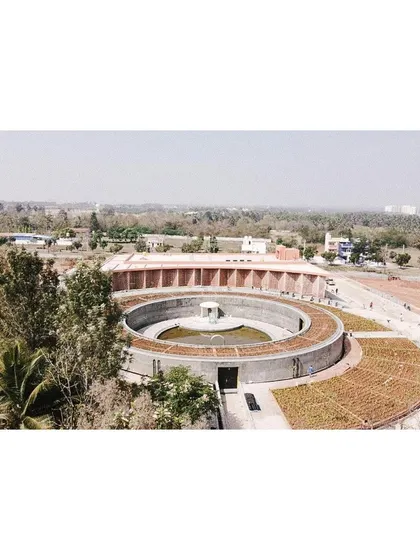 An in-progress drone shot of the memorial complex, showing the circular concrete structure of the gallery and the curved form of the auditorium taking shape. This view reveals the geometric precision of the plan before the landscape began to grow in.